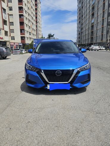 Mavi rəngli Nissan Sentra avtomobili. Avtomobilin qabaq hissəsində V