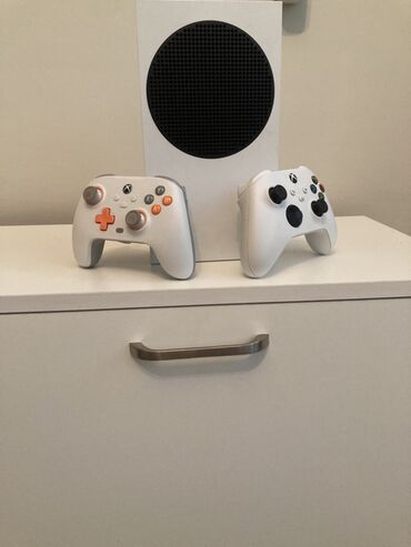 скупка телевизоров с выездом: Ağ rəngdə olan Xbox Series S oyun konsolu. Konsolun yanında iki oyun