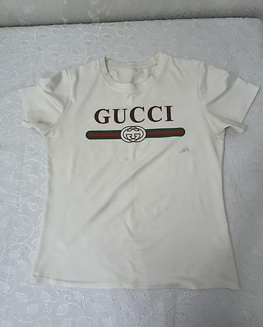 klassik geyim: Ağ rəngli qısaqol T‑shirt. Ön hissədə “GUCCI” yazısı və yaşıl‑qırmızı — 1
