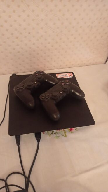 Sony PlayStation 4 Slim konsolu iki qara rəngli DualShock 4 pultu ilə