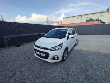арзан машинелер: Белый хэтчбек Chevrolet Spark, припаркованный на гравийной площадке