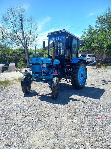 Mavi rəngli kabinəli kənd təsərrüfatı traktoru və arxadan qoşulan ot