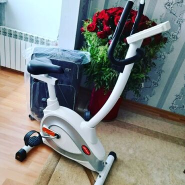 Elliptik trenajorlar: Ağ və boz rənglərdə olan stasionar velosiped trenajoru. Məşq zamanı