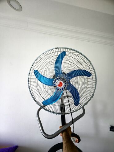 tiknti texnikasi: Mavi rəngli pərləri olan, ayaqlı, metal torlu ventilyator. Evdə və ya