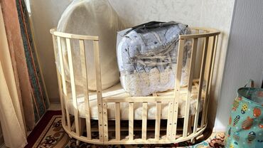 акула мягкая игрушка: Овальная деревянная детская кроватка светлого оттенка, изготовленная