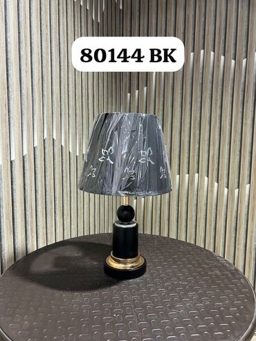 Bu masa lampası qara parça kölgəlik və qızılı rəngli metal detalları