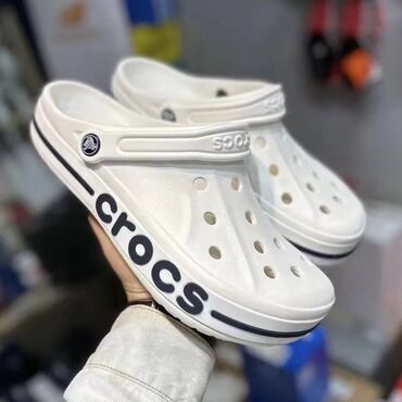 Сабо: Пара белых сабо Crocs с черной полосой вдоль подошвы и крупным