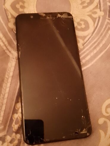 Ekranı zədələnmiş qara smartfon. Cihazın üst hissəsində, künclərdə və