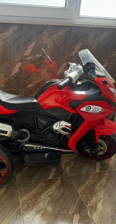 Uşaq üçün elektrik maşınları: Qırmızı rəngli, üç təkərli uşaq motosikleti. Ön hissəsində şəffaf