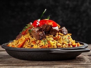 плов центр: Плов с мясом и овощами, поданный в черной сковороде. Блюдо состоит из