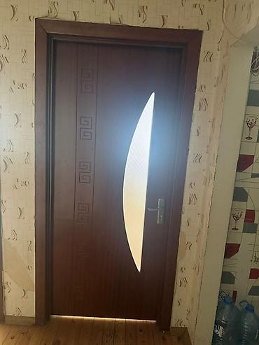 Qəhvəyi rəngli otaq qapısı. Qapının üzərində uzun, zərif formalı şüşə