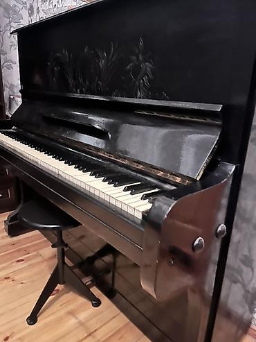 Pianolar: Upright pianino – klassik dizayn, qara rəngdə korpus. Ön paneldə — 2