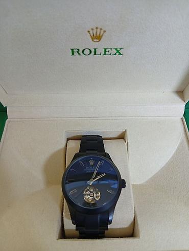 bakida saat: Rolex qol saatı – qara metal korpus və biləkli kəmər, mavi tonlarda — 1