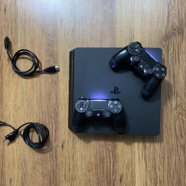 PS4 (Sony Playstation 4): Qara rəngdə olan Sony PlayStation 4 Slim oyun konsolu. Komplektə iki