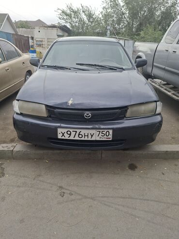 эмблема авто: Седан Mazda 323F в темно-синем цвете, оснащенный литыми дисками и