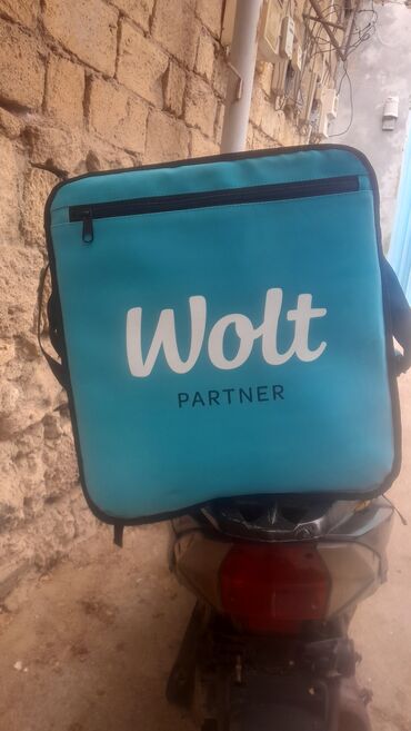 Qril aparatları: Wolt loqosu və "PARTNER" yazısı olan mavi rəngli çatdırılma çantası