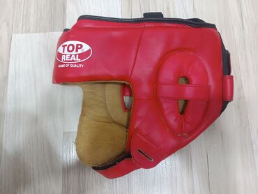 Turniklər və bruslar: Qırmızı rəngdə "TOP REAL" markalı boks başlığı. Bu başlıq, məşq və ya