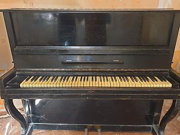 Upright piano – klassik qara korpuslu, dekorativ oyma panellərlə. -