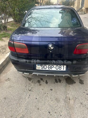 maşin bazar: Tünd göy rəngli Opel Omega sedanı. Arxa tərəfində dörd ədəd egzos