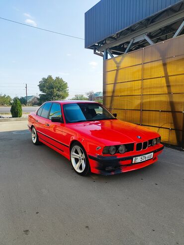 эмблема авто: Красный седан BMW E34 с черными молдингами и тонированными стеклами