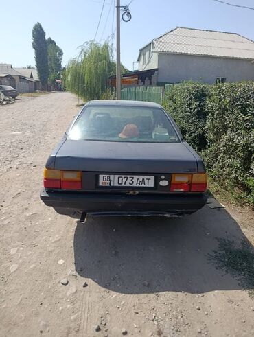 очки фирменные: Седан Audi 100 темно-серого цвета, видны следы износа. Автомобиль