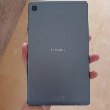 ses sisdemi: Arxa tərəfində "SAMSUNG" loqosu olan boz rəngli bir planşet. Onun arxa