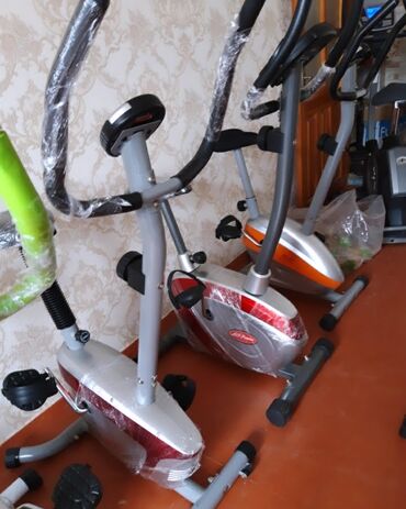 qaçış trinajoru: Qırmızı və gümüşü rəngli, qolları olan stasionar velosiped trenajoru