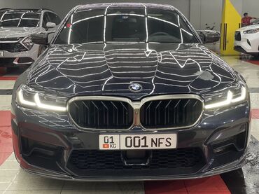 BMW: Автомобиль BMW M5 в кузове седан, окрашенный в темный цвет. Он оснащен