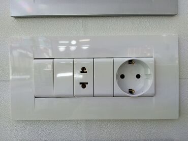 tek guzgu: Ağ rəngli, geniş çərçivəli elektrik rozetka və açar paneli. Paneldə