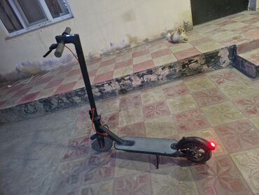 Samokatlar: Qara rəngdə, elektrikli skuter. Sükanın mərkəzində sürət və digər
