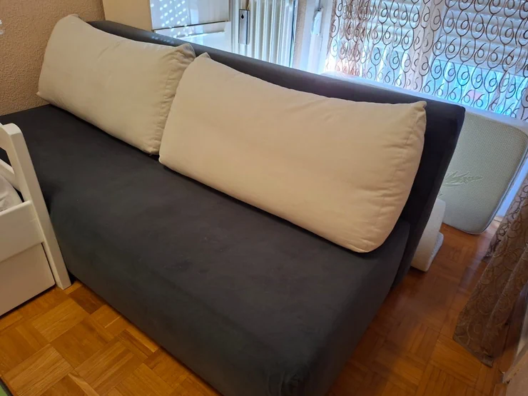 Sofa tamnosive boje sa dva svetla jastuka, idealna za dnevni boravak